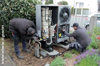 Hybridheizung Ober-Mörlen Zwei Heizungstechniker montieren eine neue Wärmepumpe im Vorgarten eines Wohnhauses